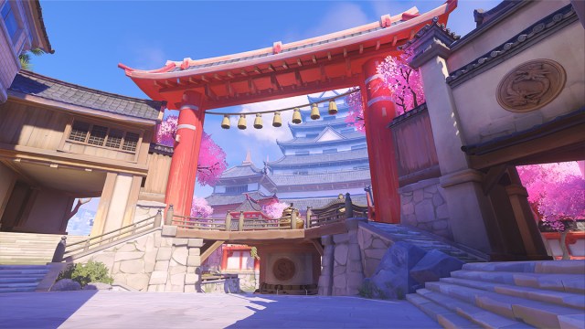 Screenshot from Overwatch 2 of the Hanaoka map. It's bright daytime with cherry blossom trees and Japanese architecture in the background, framed by a gate.