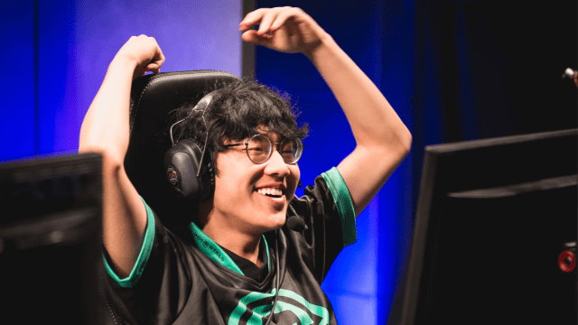 LCS IMT player Olleh sits in a chair in front of a monitor with a big smile, hands above his head